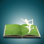 Paper cut of girl doing yoga on old book grass